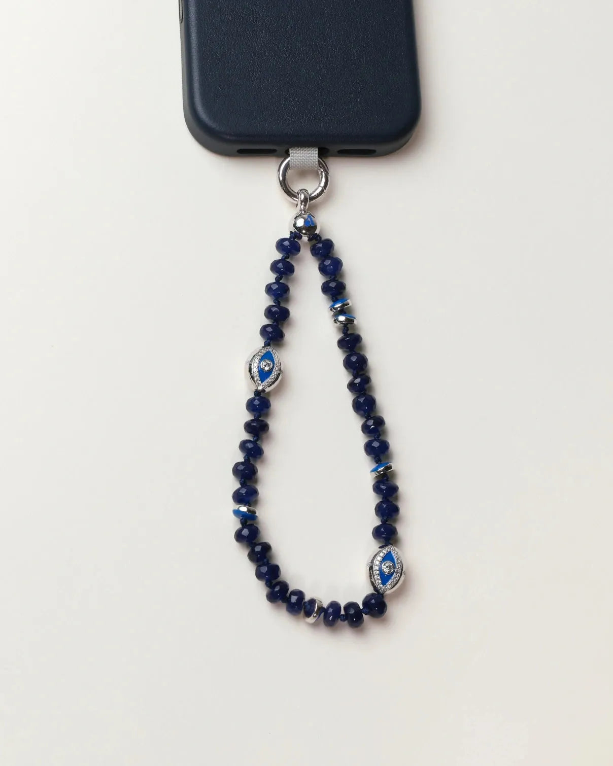 Overhead shot of the Sapphire Leah Phone Charm on a white background, featuring sapphire-toned beads and protective evil eye charms.