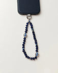 Overhead shot of the Sapphire Leah Phone Charm on a white background, featuring sapphire-toned beads and protective evil eye charms.