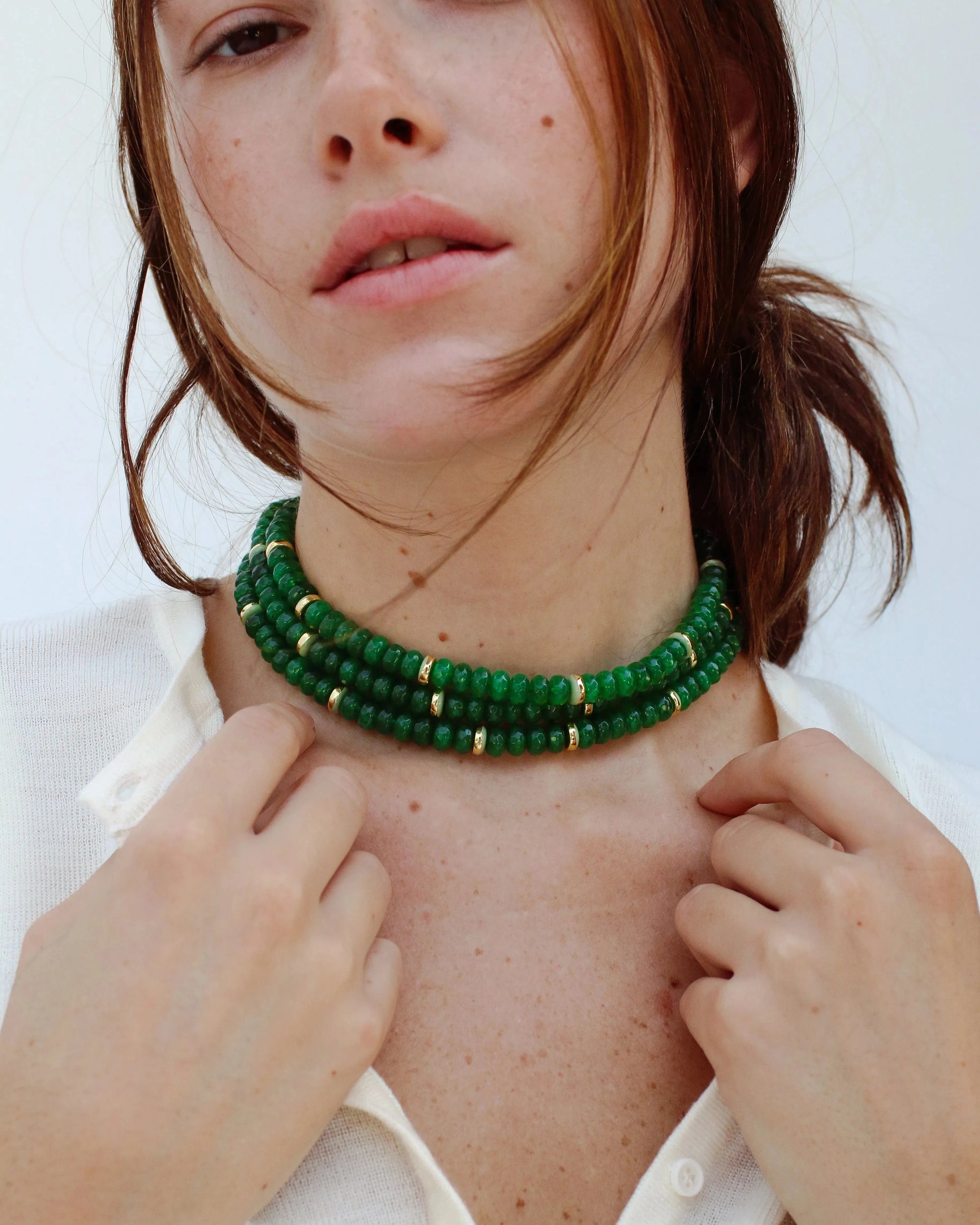 Woman wearing the lilou emerald beaded necklace with gold accents, styled with a light cream cardigan. The jewelry showcases vibrant green quartz beads, emphasizing elegance and balance.