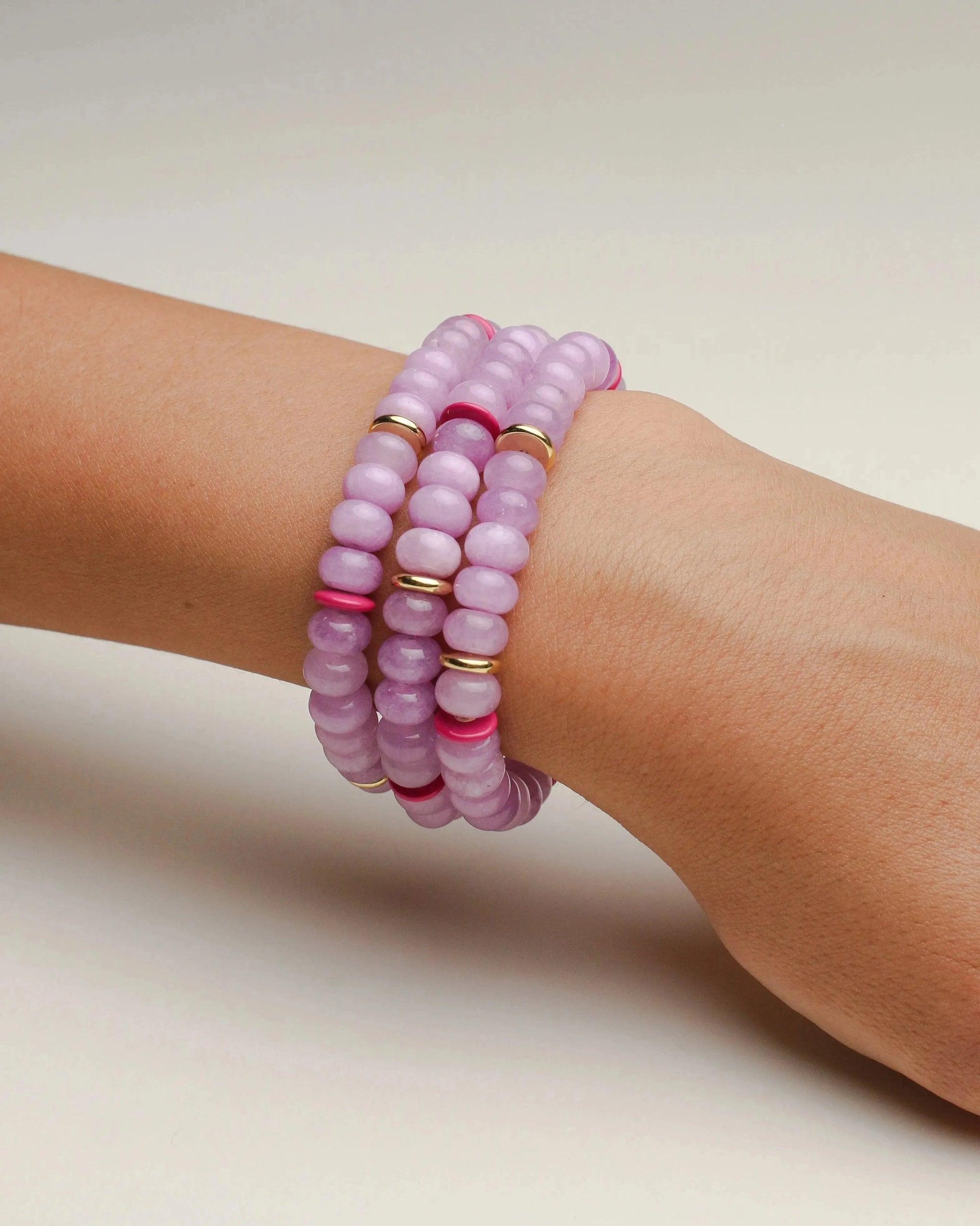 A set of three valerie lavender bracelets worn on the wrist, featuring soft purple beads with pink and gold accent dividers, offering a stylish, layered look.
